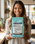 Woman holding a Selden & Kingsley Coffee package in a bright, modern cafe.
